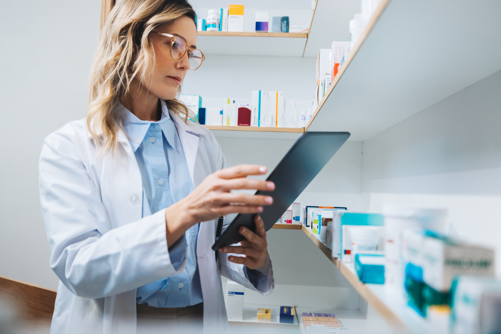 Female pharmacist standing in a pharmacy looking at a tablet.