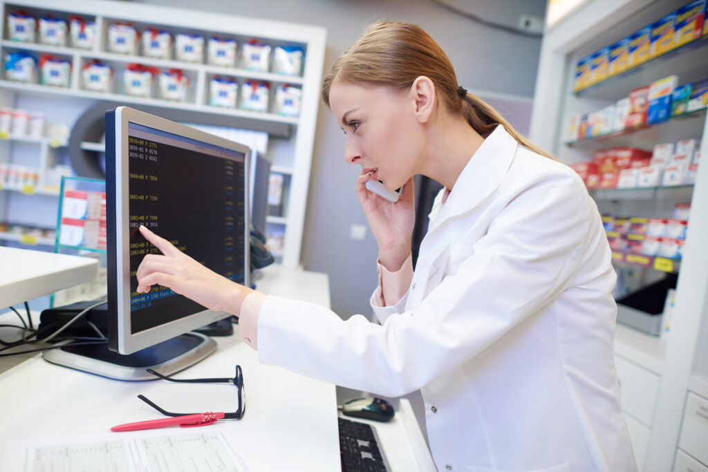 A female pharmacist frowns looking closely at a computer monitor.
