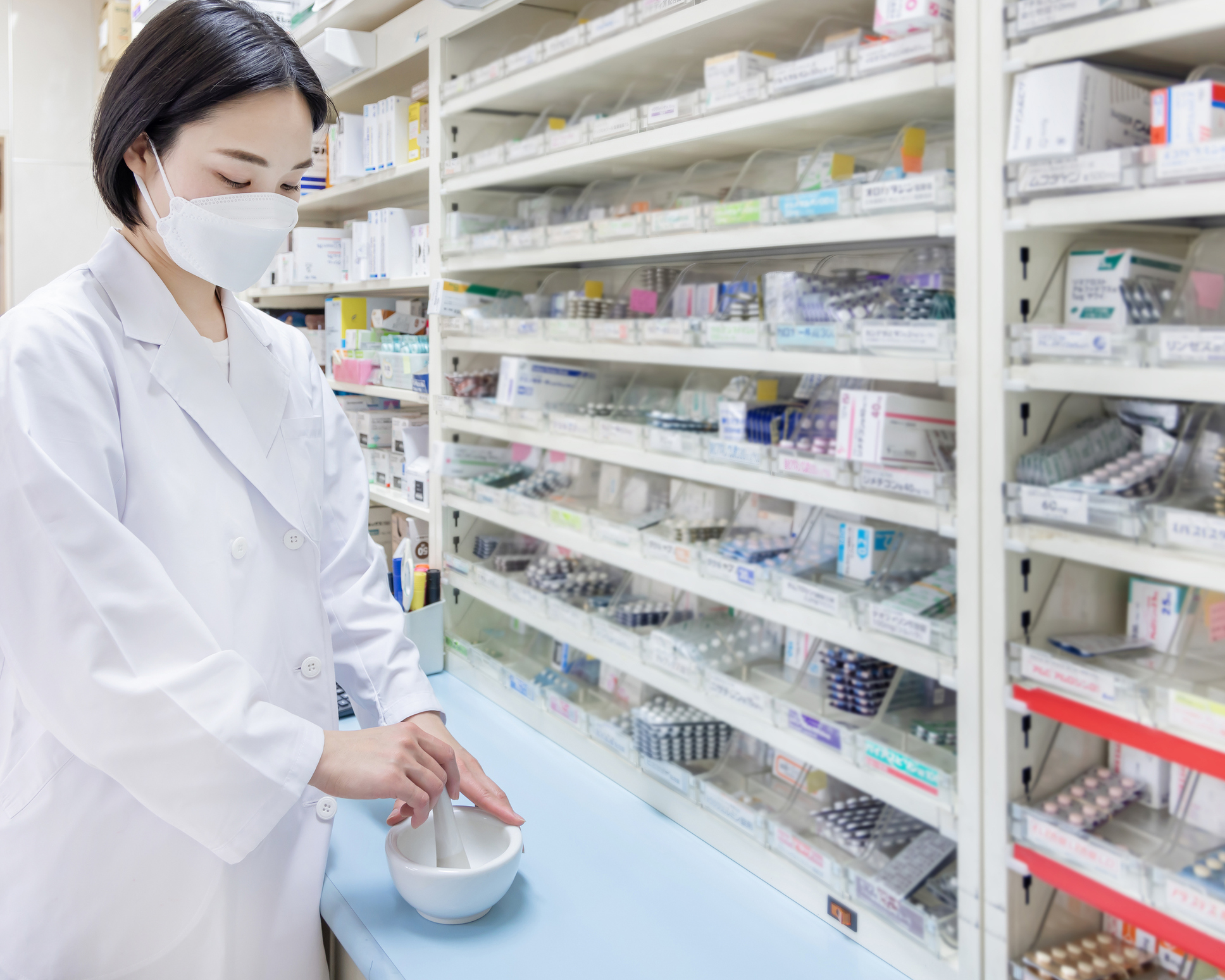 A female pharmacist wears a mask while she customizes a prescription.