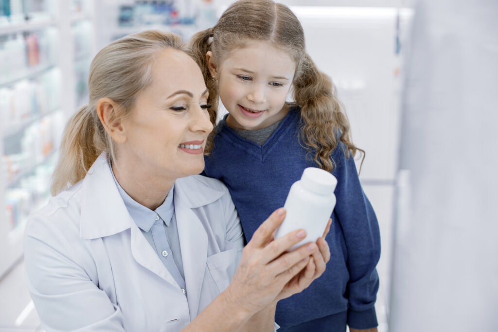A smiling female pharmacist shows a young girl her medication.