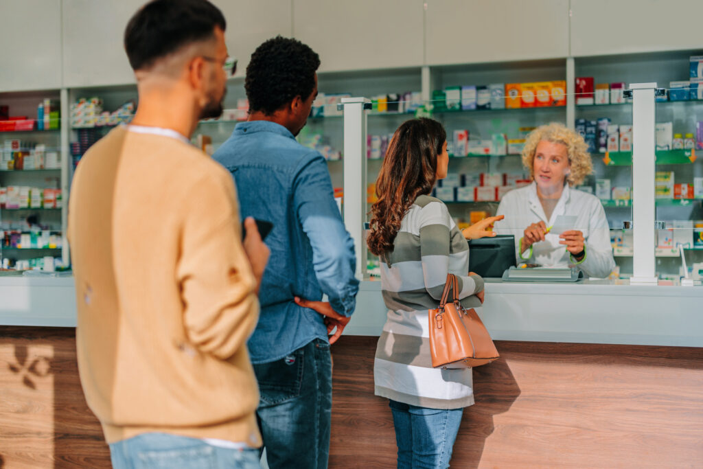 A small line wait to speak to a pharmacist standing behind the counter. 