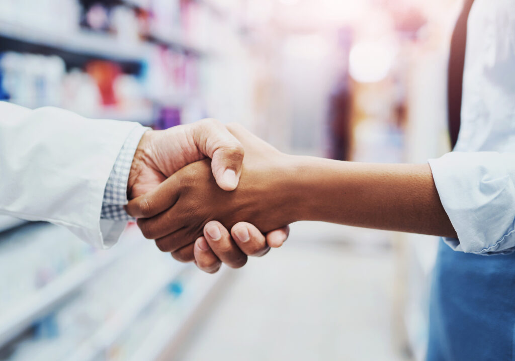 Two pharmacists are shaking hands in a pharmacy.