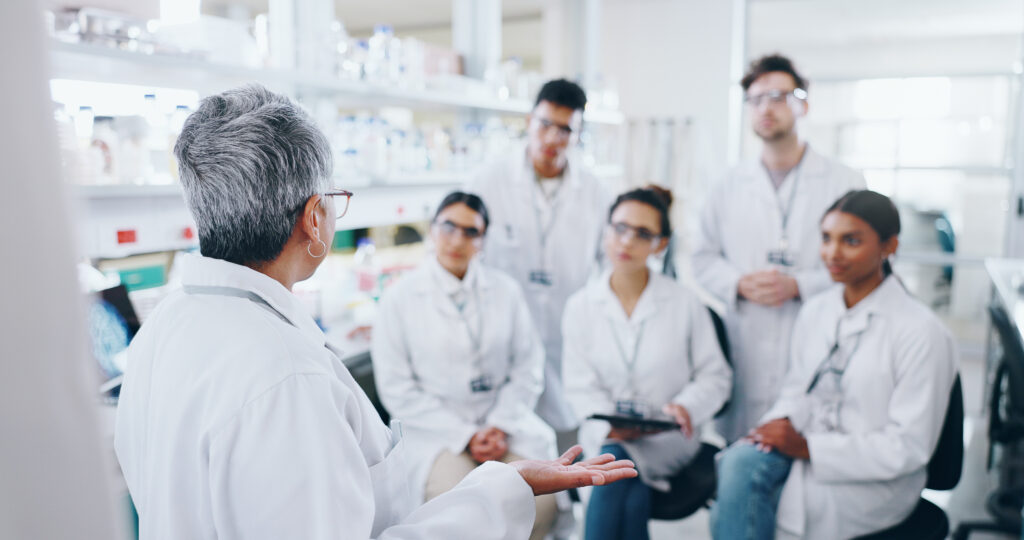 An older female pharmacist meets with a group of younger pharmacists. 