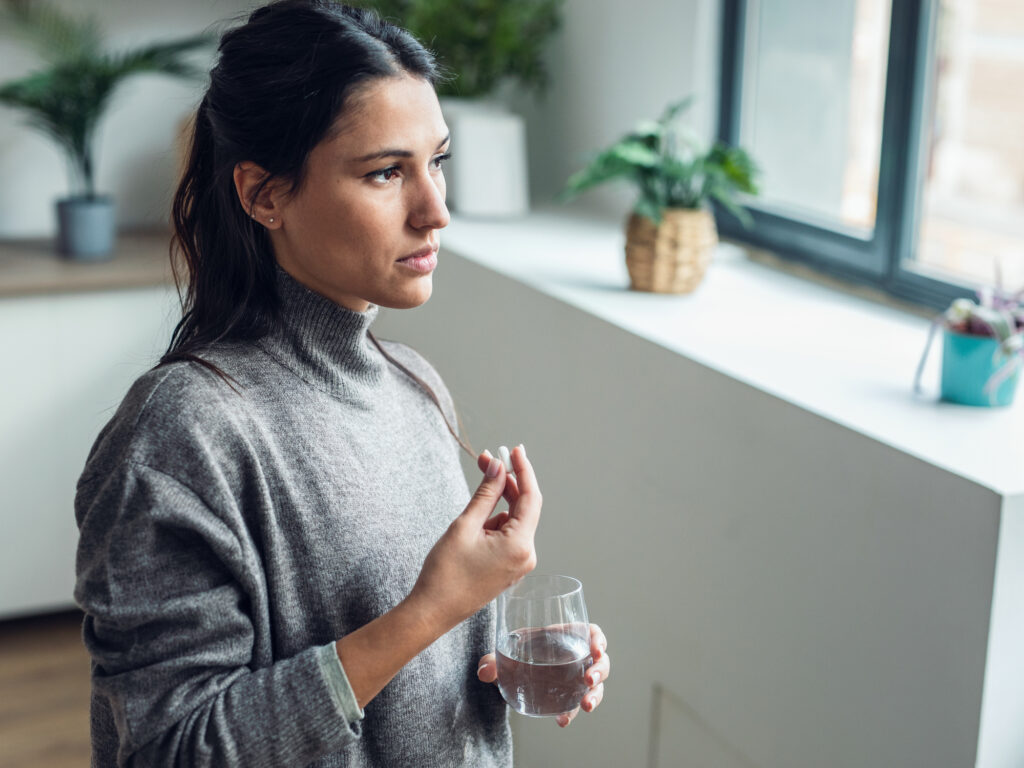 A young woman prepares to take her medication with a glass of water. 