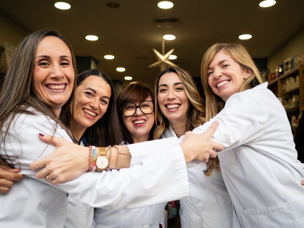 A group of female pharmacists stand together embracing and smiling.