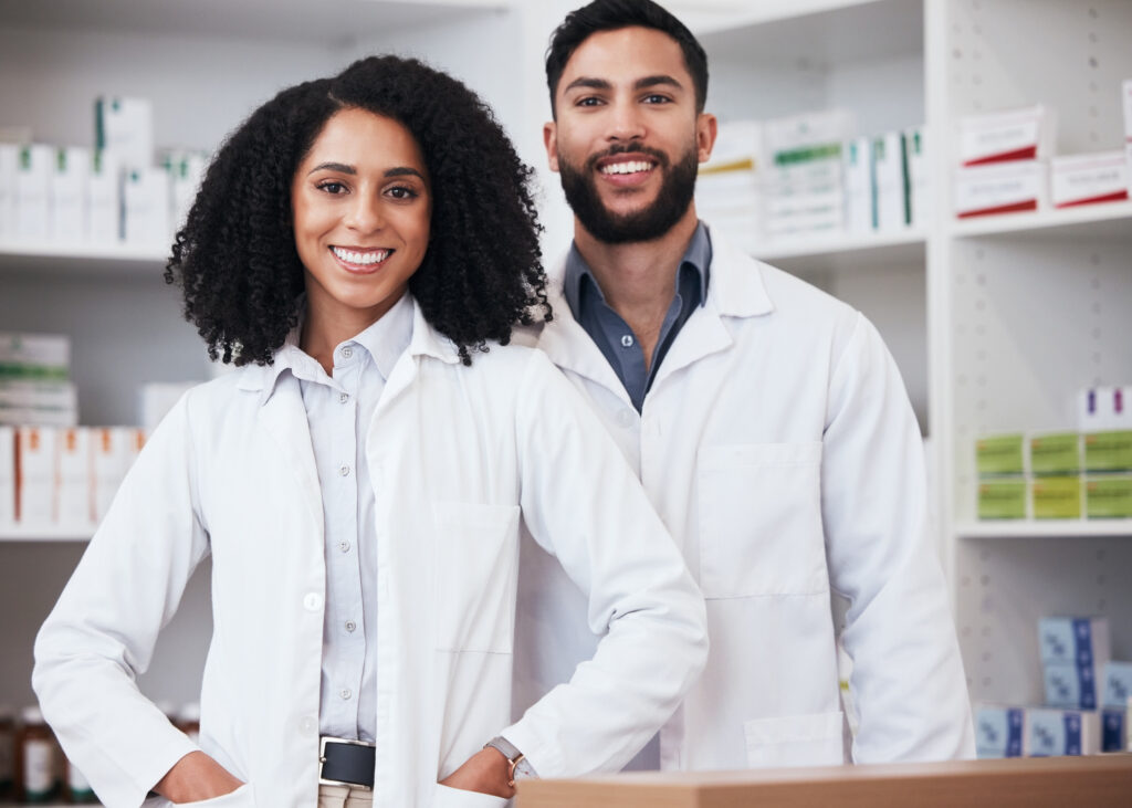 A male and female pharmacist stand side-by-side smiling. 