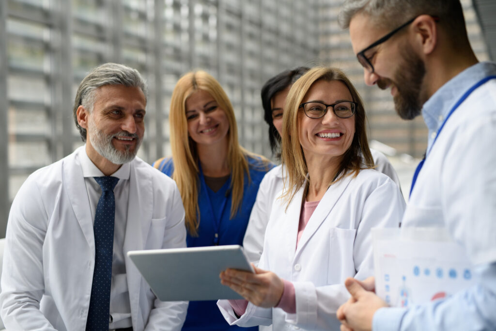 A group of smiling male and female pharmacists stand together reviewing information on a tablet.