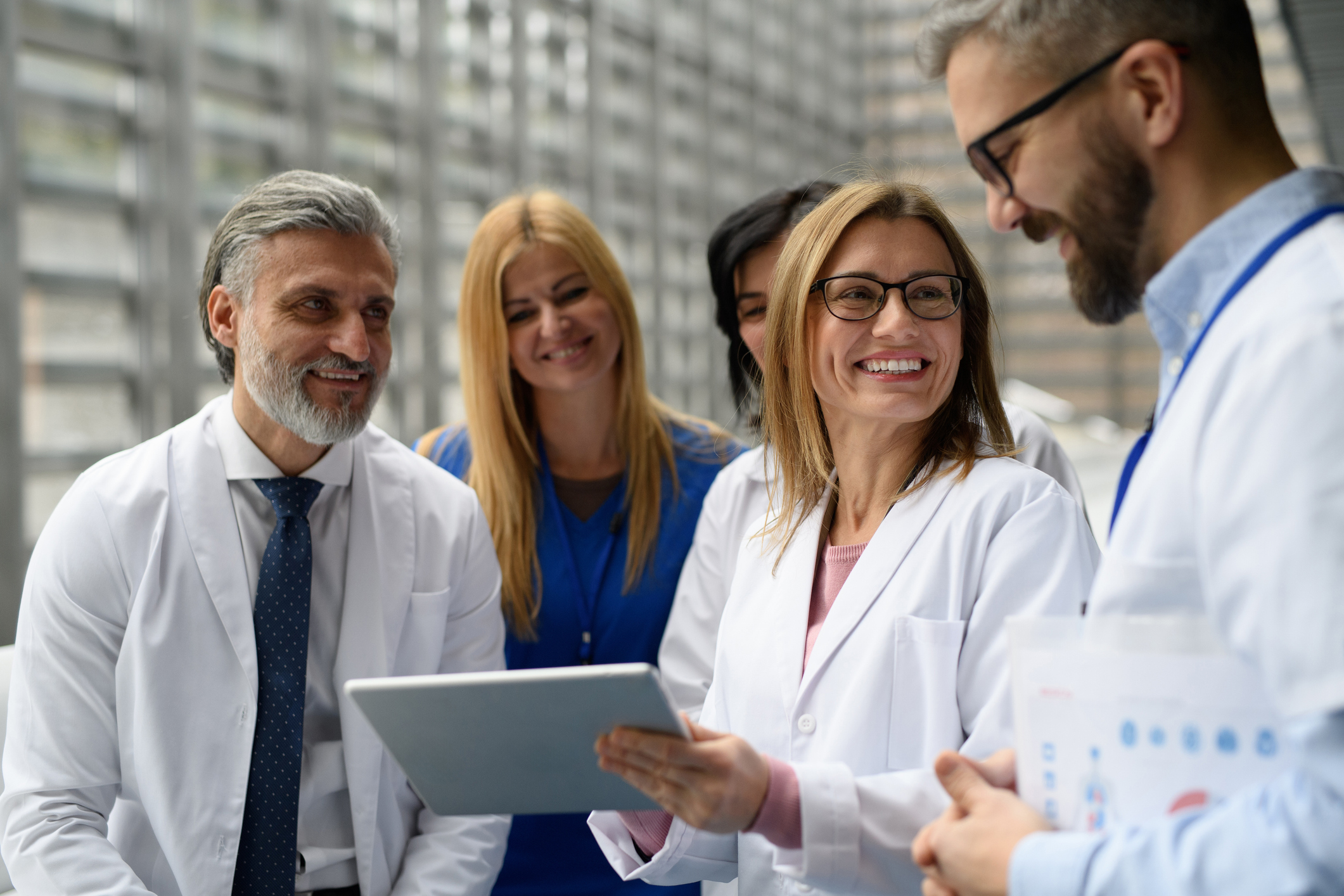 A group of smiling male and female pharmacists stand together reviewing information on a tablet.