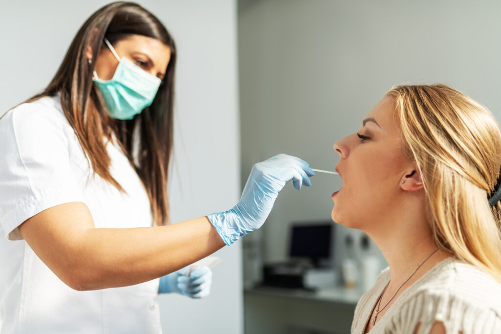 A female healthcare worker wears a mask and gloves while swabbing a woman's cheek.