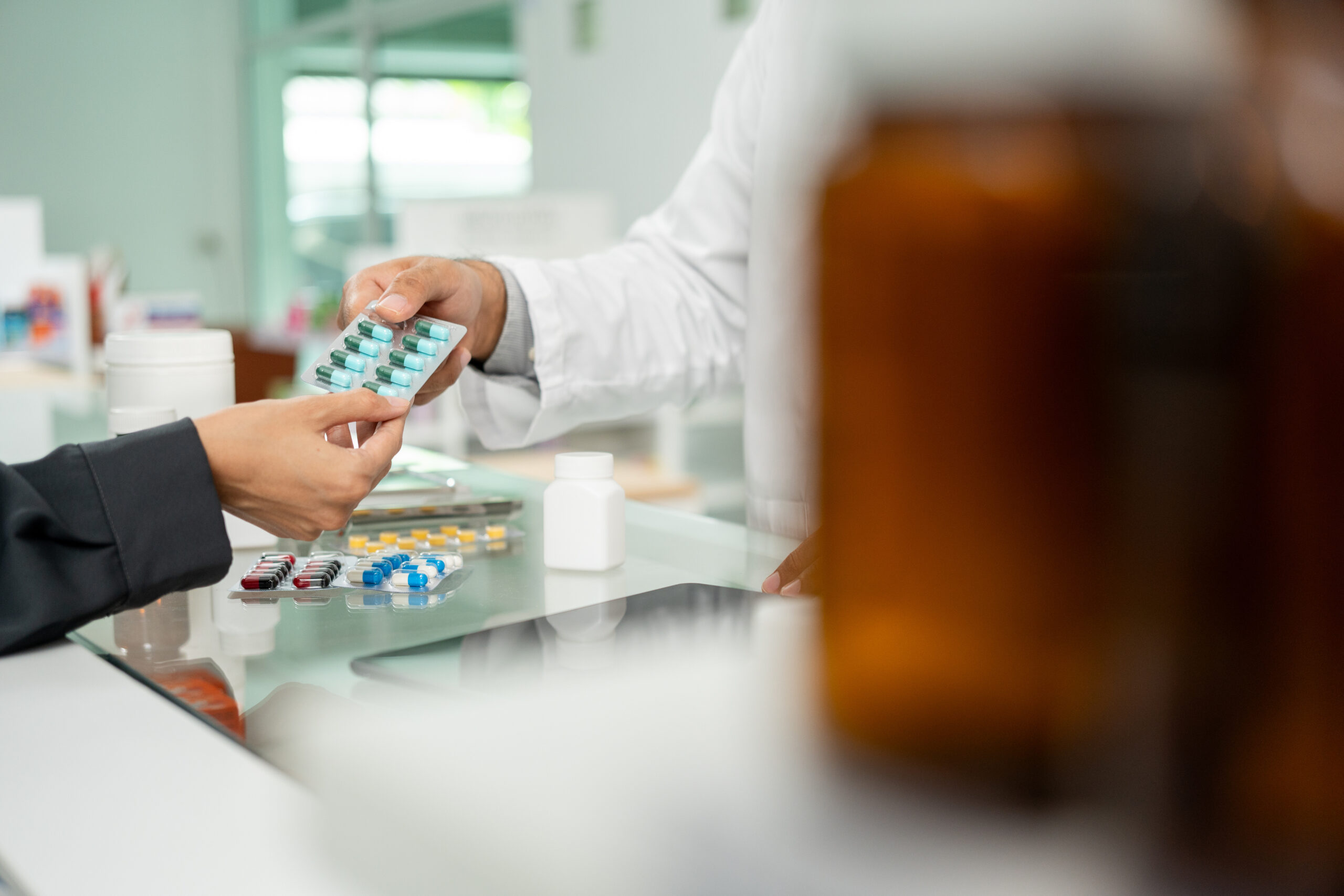 A pharmacist hands a medication package to a patient at the counter.