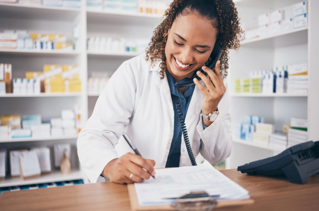 A female pharmacist is smiling while on a call with a patient.